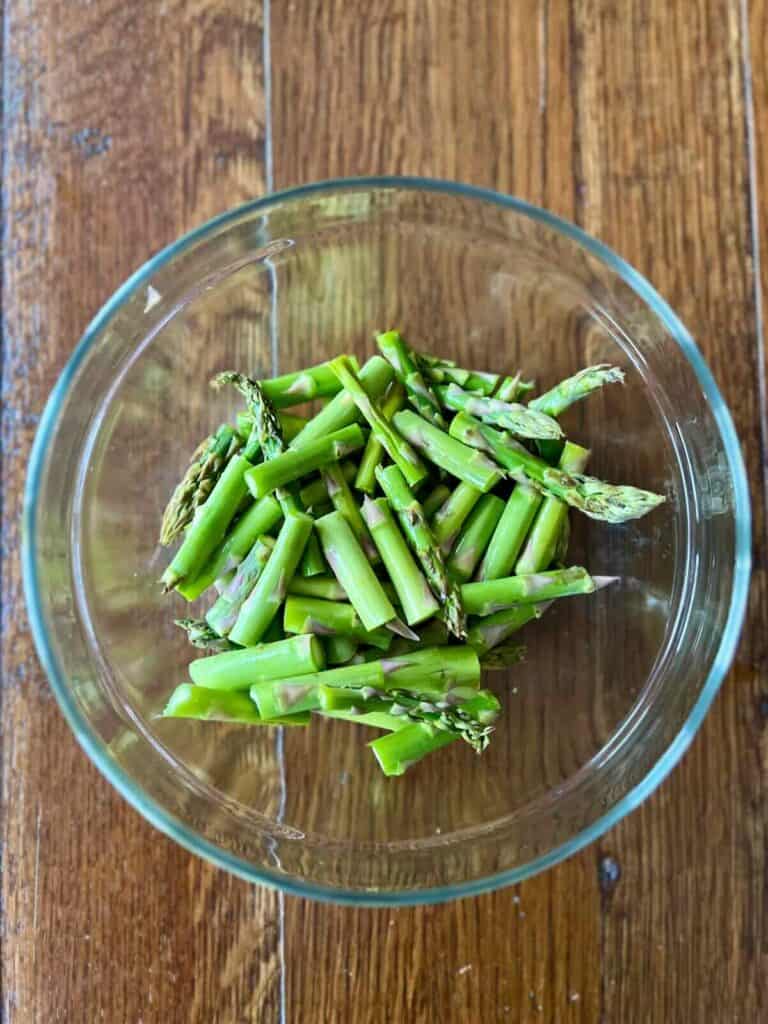 round glass bowl of asparagus chunks with tamari on a wood table