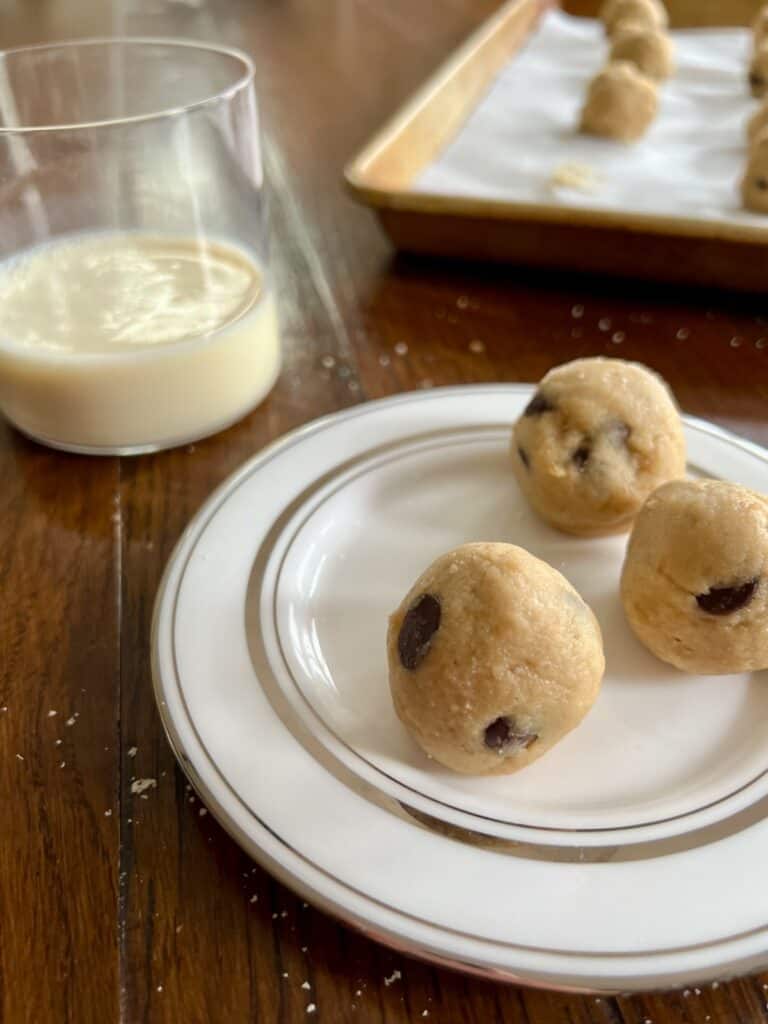 small plate of three banana bread cookie dough freezer bites with a glass of milk and baking sheet in the background