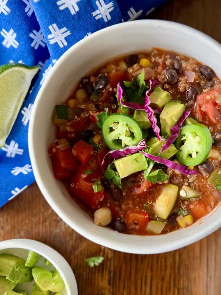 close up overhead of bowl of zesty quinoa chili garnished with jalapeño slices, purple cabbage, diced avocado, and cilantro