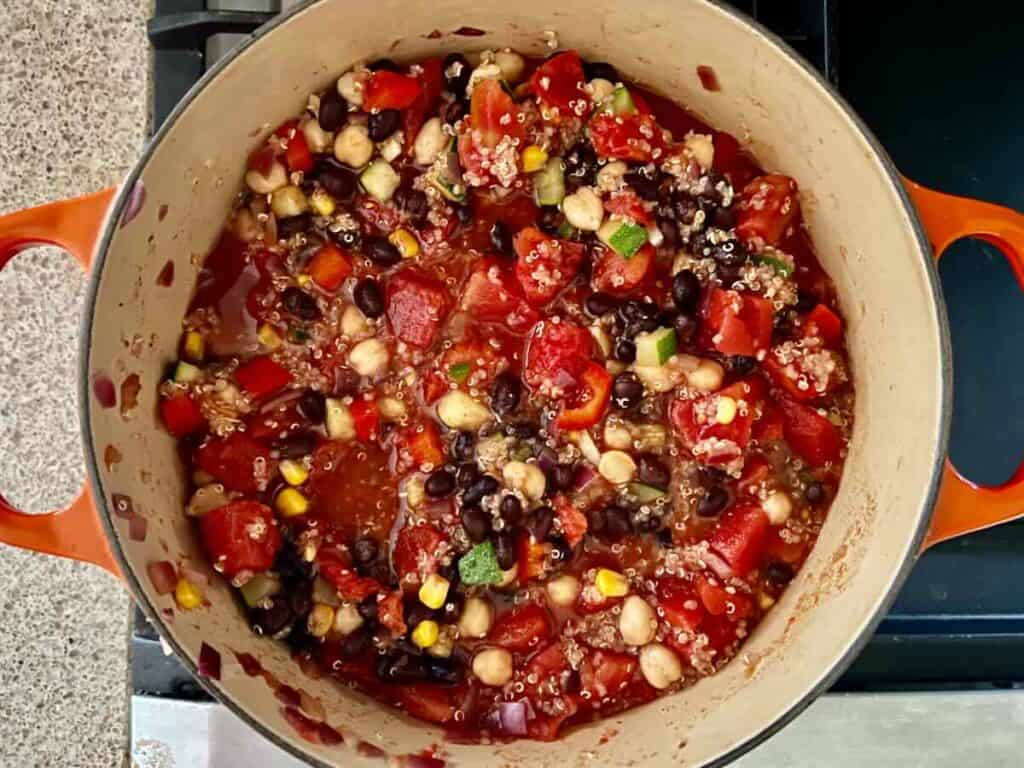 overhead view of Dutch oven containing cooked vegetable and spice mixture with added tomatoes, black beans, and chickpeas