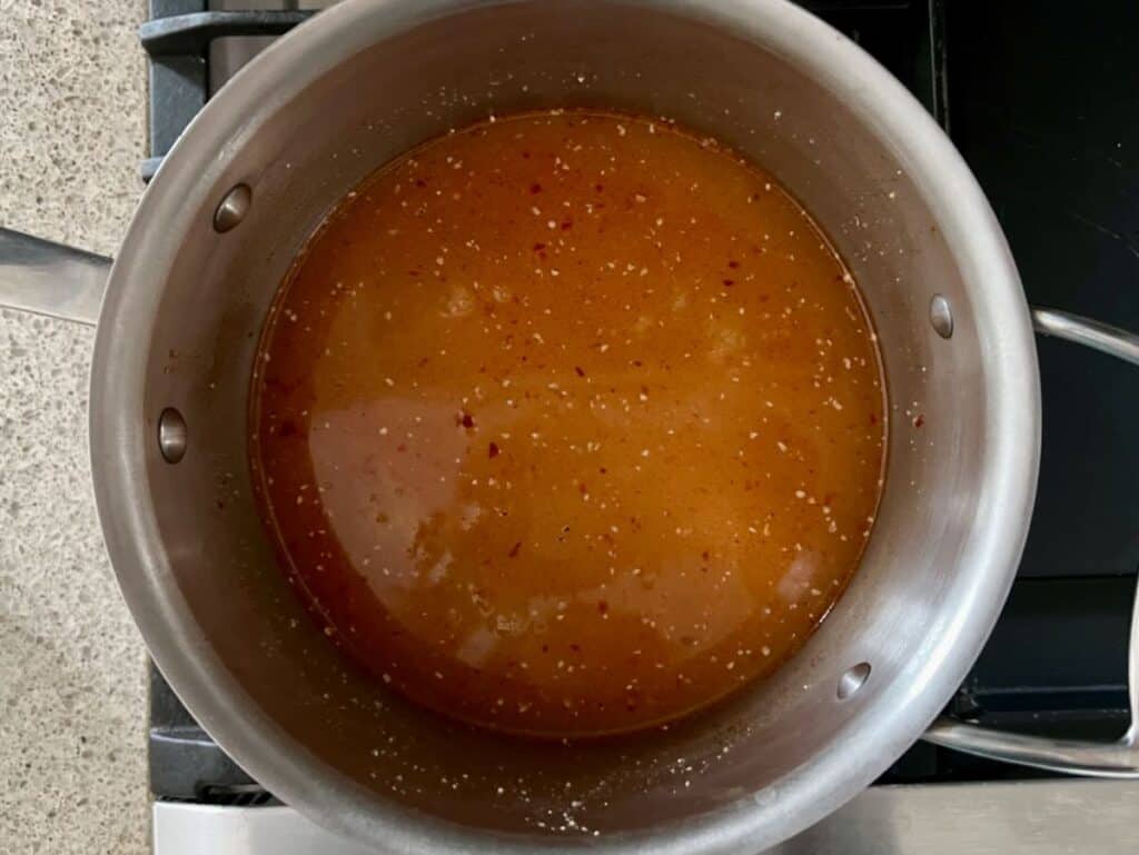 stainless steel pot containing water, uncooked polenta, and harissa on a stove