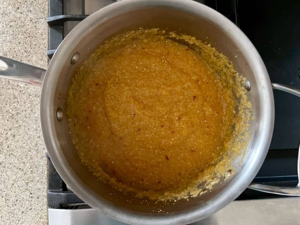 stainless steel pot containing water, cooked polenta, and harissa on a stove