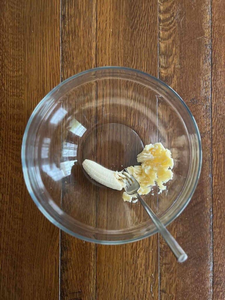 overhead view of glass bowl with fork partially mashing a banana