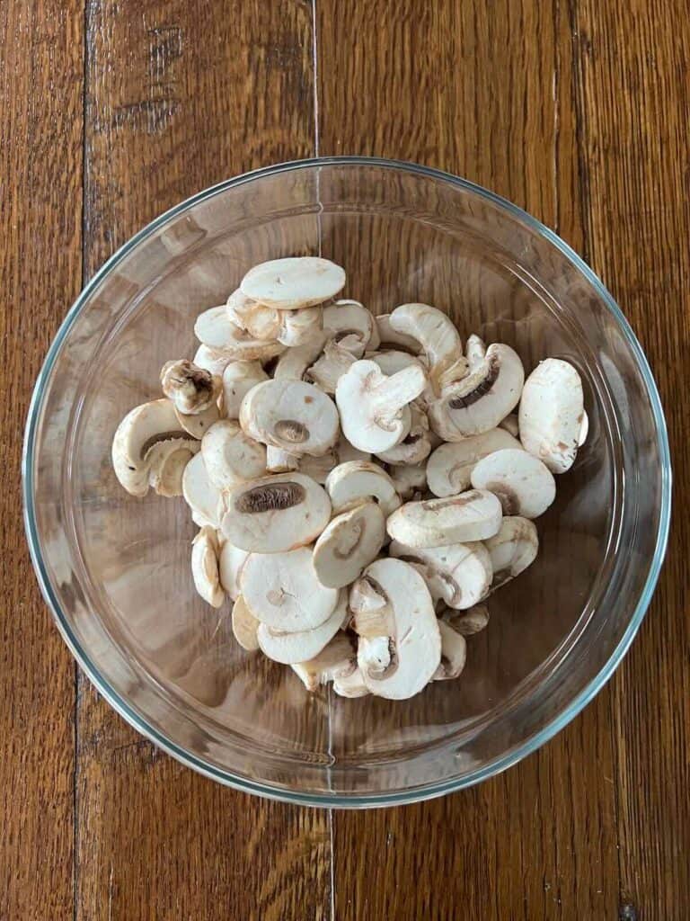 round glass bowl of sliced button mushrooms with tamari on a wood table