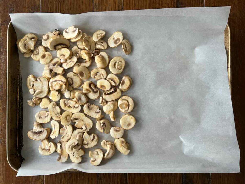 metal baking sheet lined with parchment paper with sliced mushrooms on left side