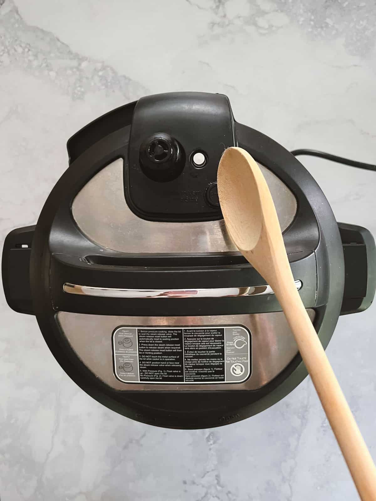 overhead view of Instant Pot with wooden spoon pressing the Pressure Release knob