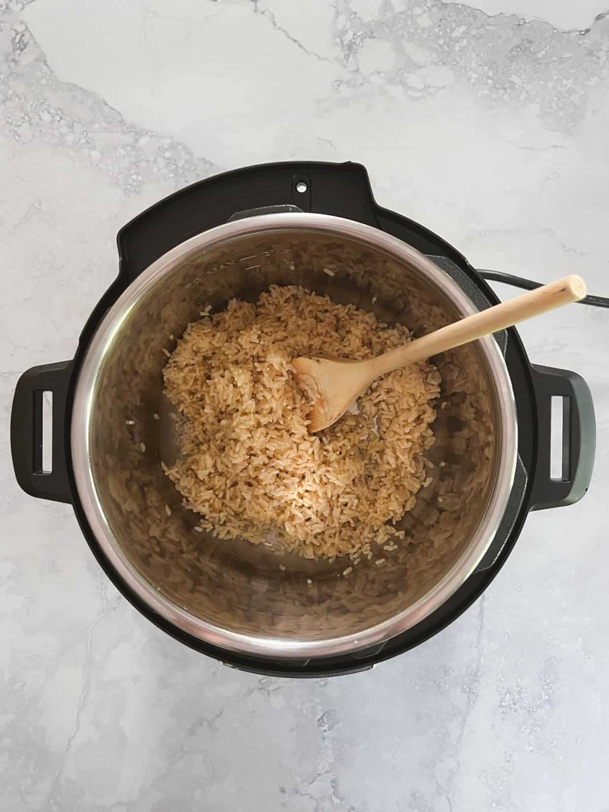 overhead view of Instant Pot containing brown rice with wooden spoon fluffing the rice