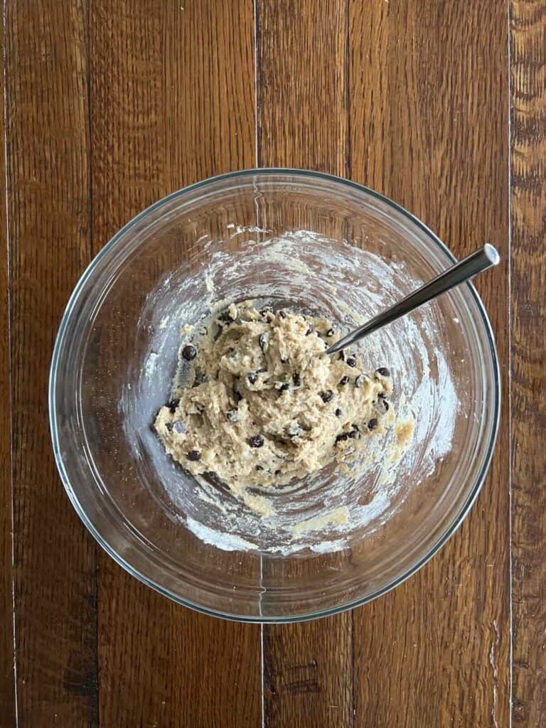 overhead view of glass bowl containing wet and dry ingredients mixed, with chocolate chips stirred in