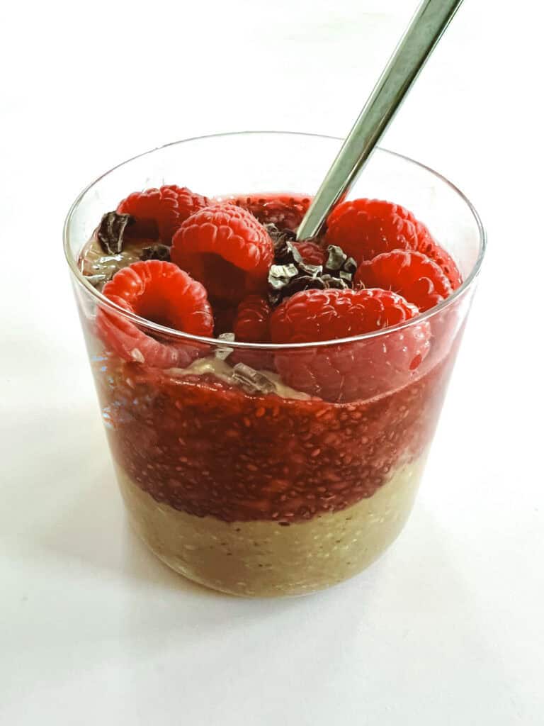 close up of glass of creamy layered cocoa raspberry overnight oats with spoon