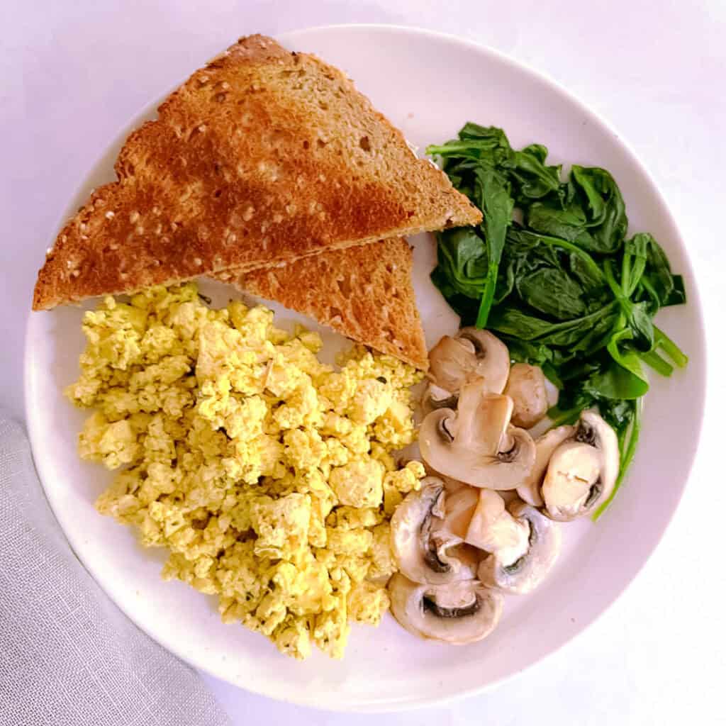herbed tofu scramble on a plate with mushrooms, spinach, and toast