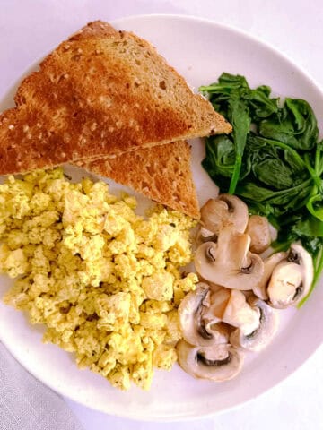 herbed tofu scramble on a plate with mushrooms, spinach, and toast