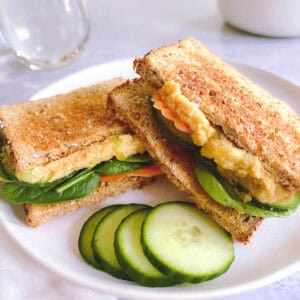 sliced vegan tuna salad sandwich on a plate with sliced cucumbers