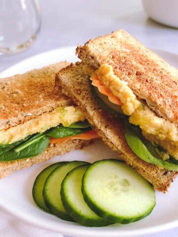 sliced vegan tuna salad sandwich on a plate with sliced cucumbers