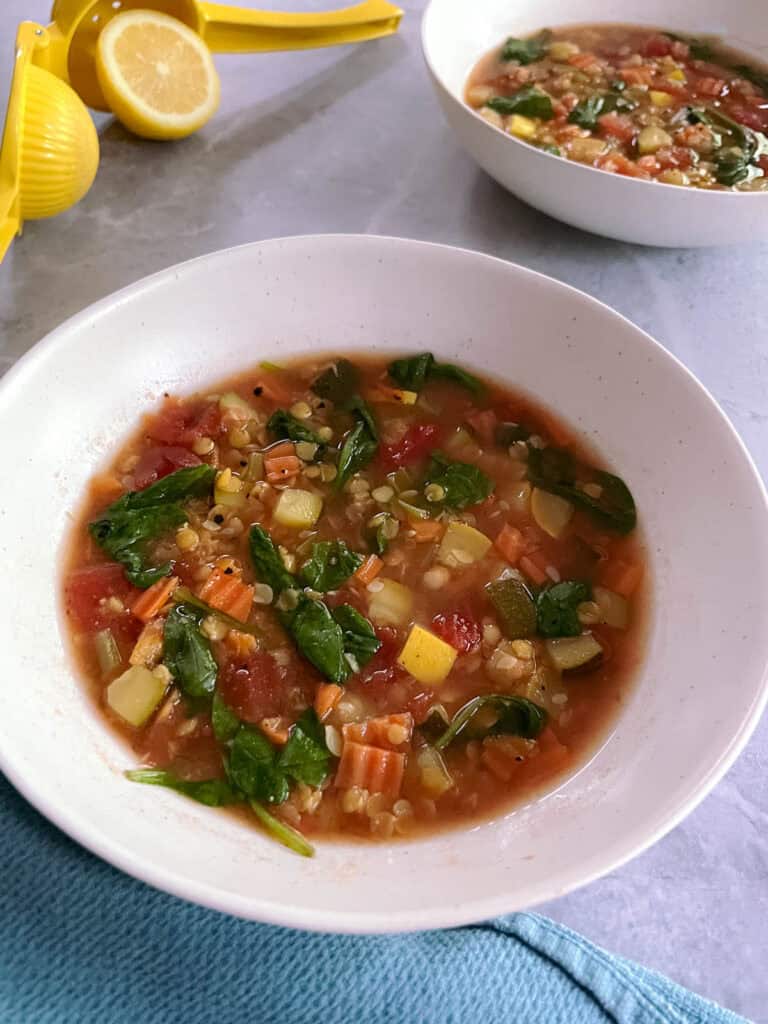 two bowls of simple red lentil minestrone soup with sliced lemon