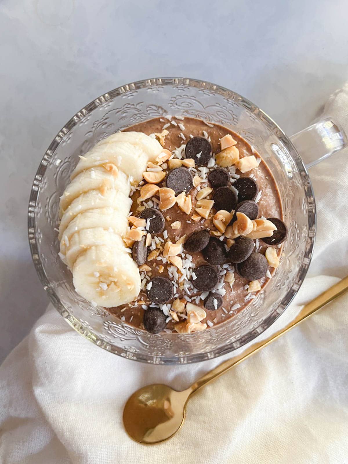 overhead view of glass mug containing creamy blended chocolate peanut butter overnight oats with toppings and gold spoon