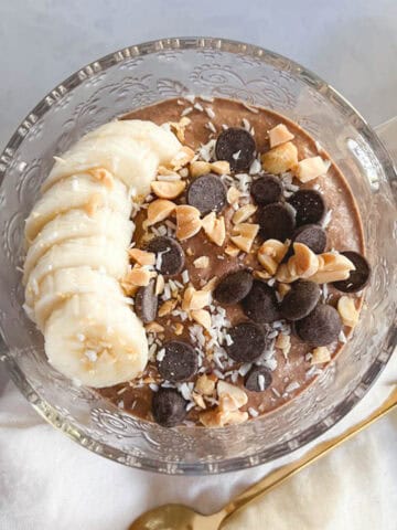 bowl of creamy chocolate peanut butter overnight oats topped with bananas, chocolate chips, shredded coconut, and crushed peanuts