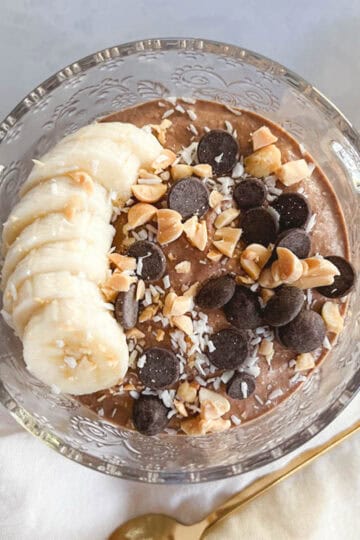 bowl of creamy chocolate peanut butter overnight oats topped with bananas, chocolate chips, shredded coconut, and crushed peanuts