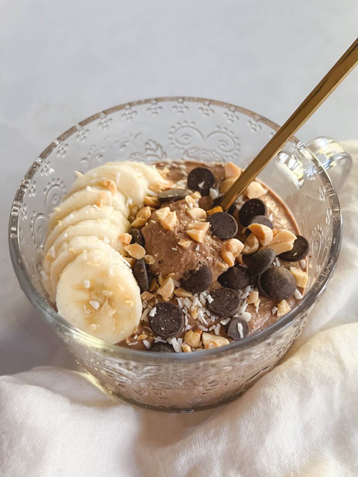 glass mug of creamy blended chocolate peanut butter overnight oats with gold spoon digging in