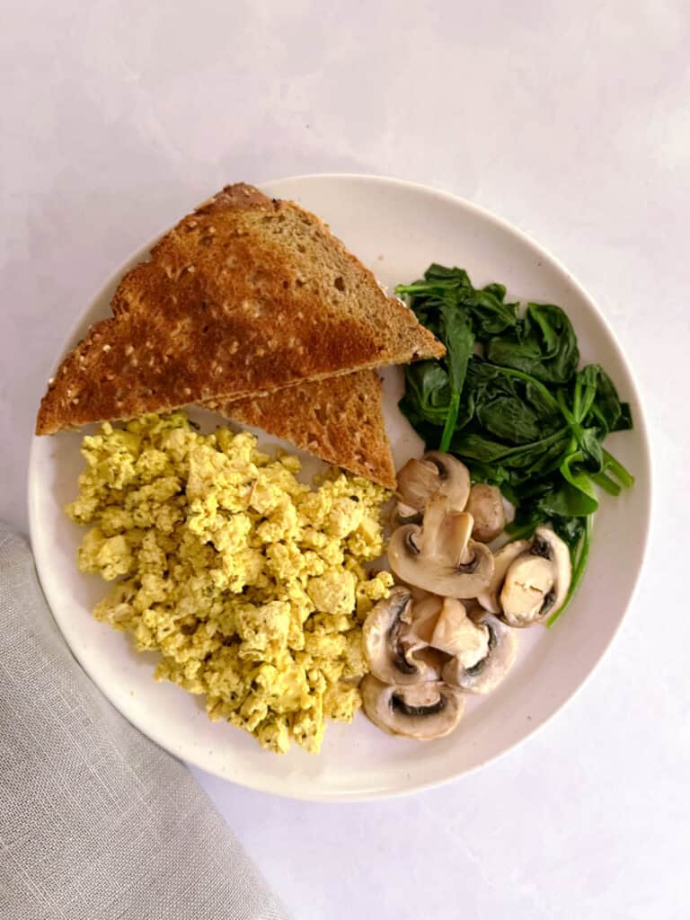 plate containing herbed tofu scramble, toast, sautéed spinach, and sliced mushrooms