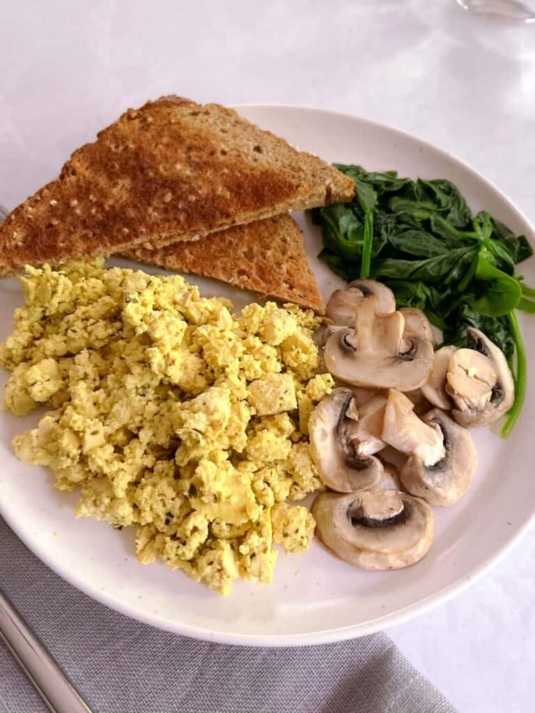 plate of herbed tofu scramble with toast, sautéed spinach, and mushrooms