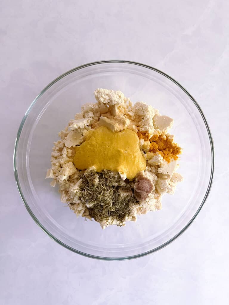 bowl containing crumbled tofu, nutritional yeast/milk blend, and other seasoning ingredients