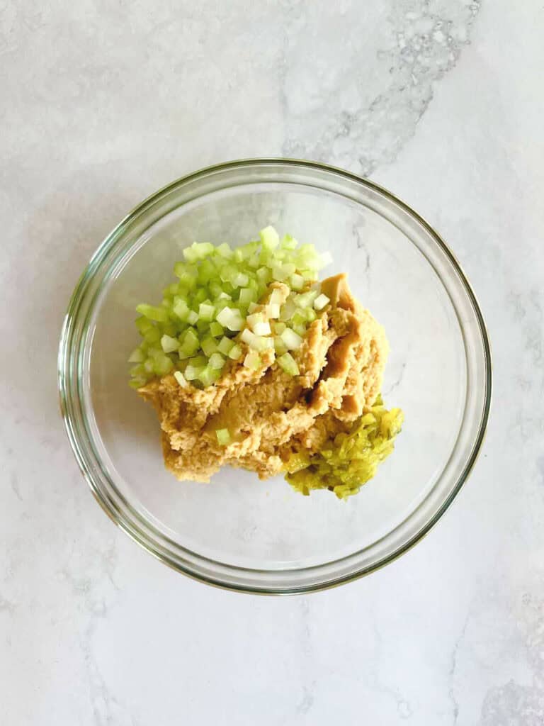 overhead of glass bowl containing chickpea mixture, pickle relish, and celery