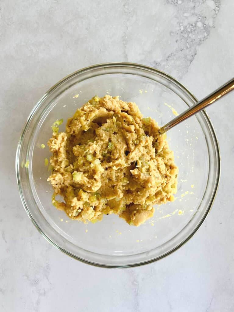 glass bowl containing chickpea mixture with pickle relish and celery, mixed with a spoon