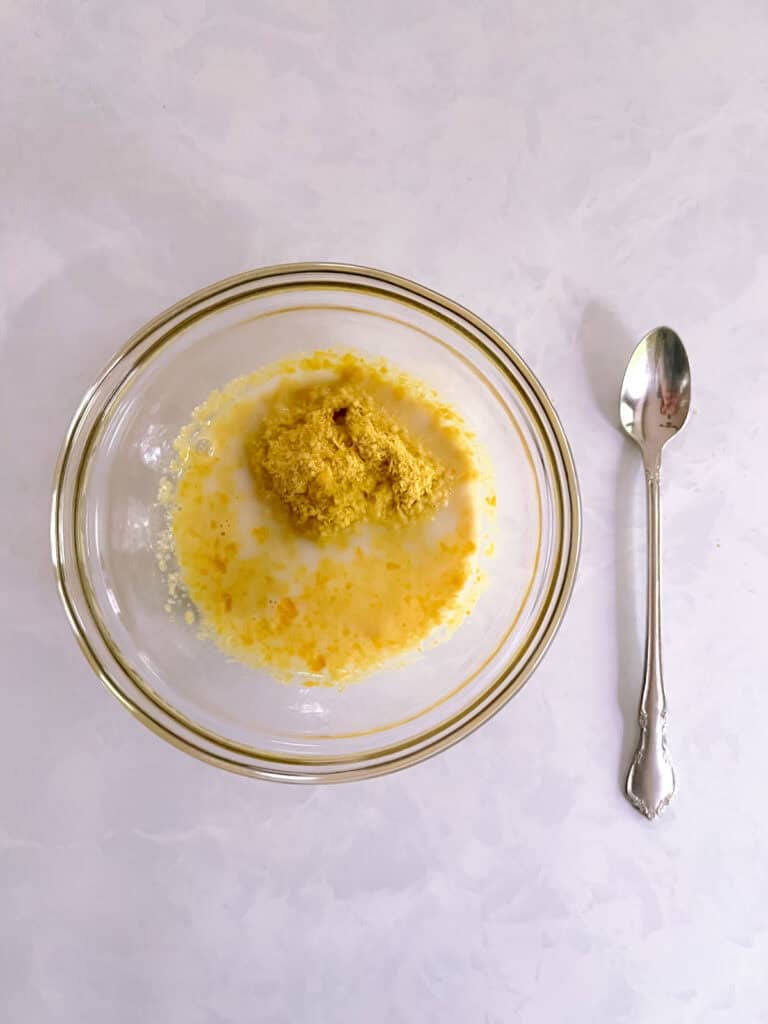 small bowl containing unblended nutritional yeast and nondairy milk with spoon on the right