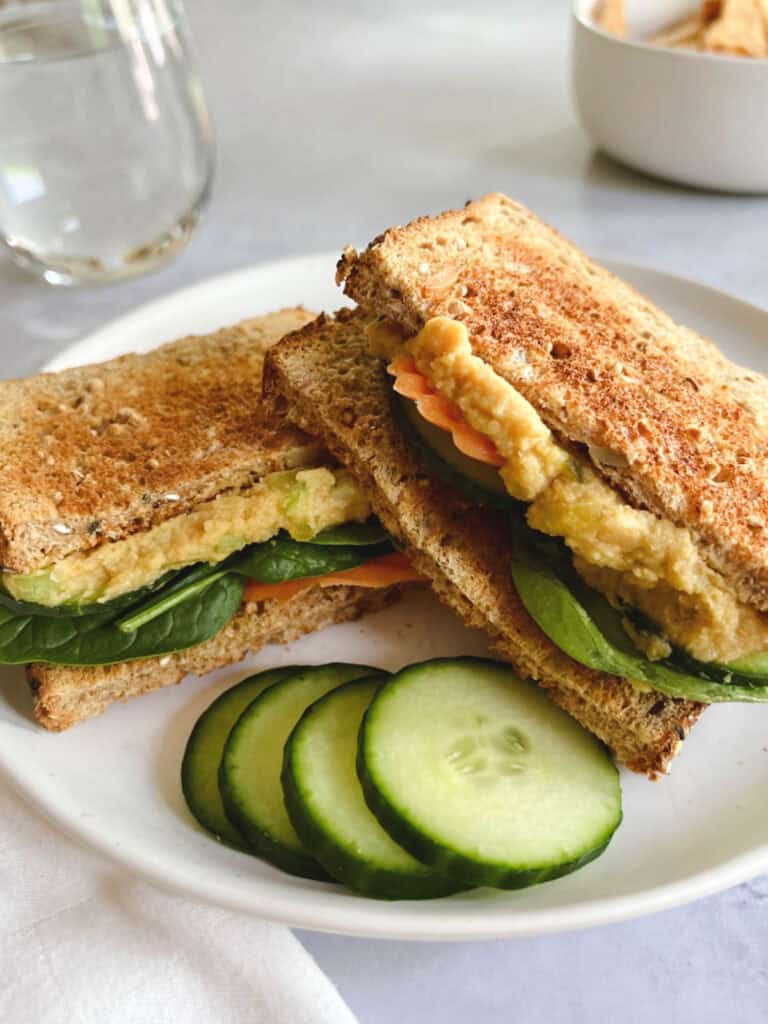 plate with vegan tuna salad sandwich sliced in half with cucumbers