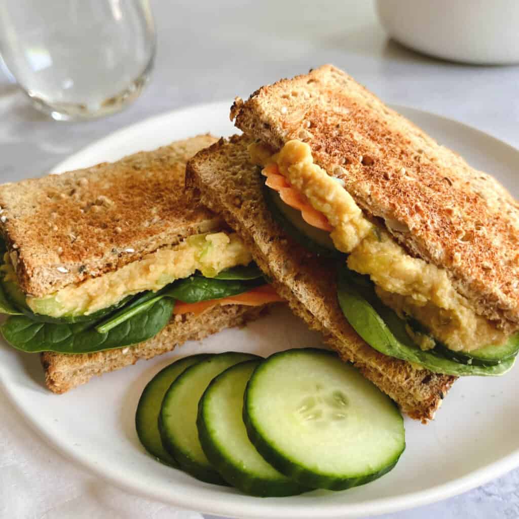 vegan tuna salad sandwich sliced in half on a plate with sliced cucumbers