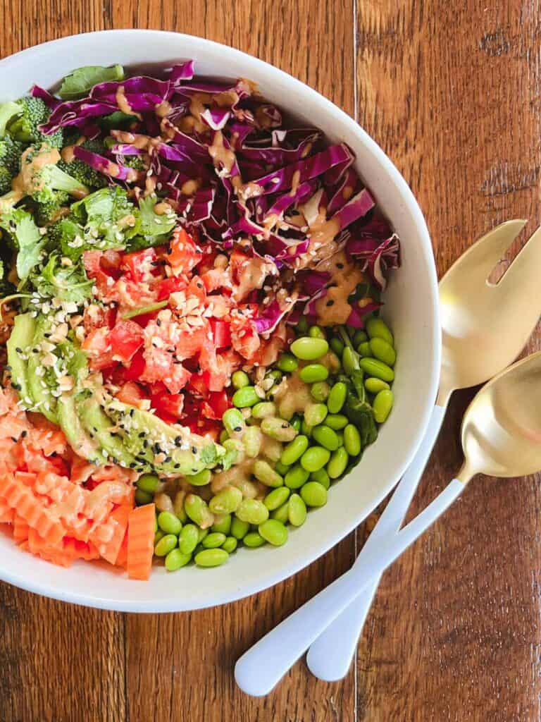 large bowl of easy rainbow crunch edamame salad with tangy peanut dressing with serving utensils on the side