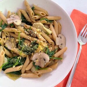 spinach, mushroom, and artichoke pasta with a fork and napkin