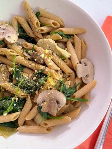 spinach, mushroom, and artichoke pasta with a fork and napkin