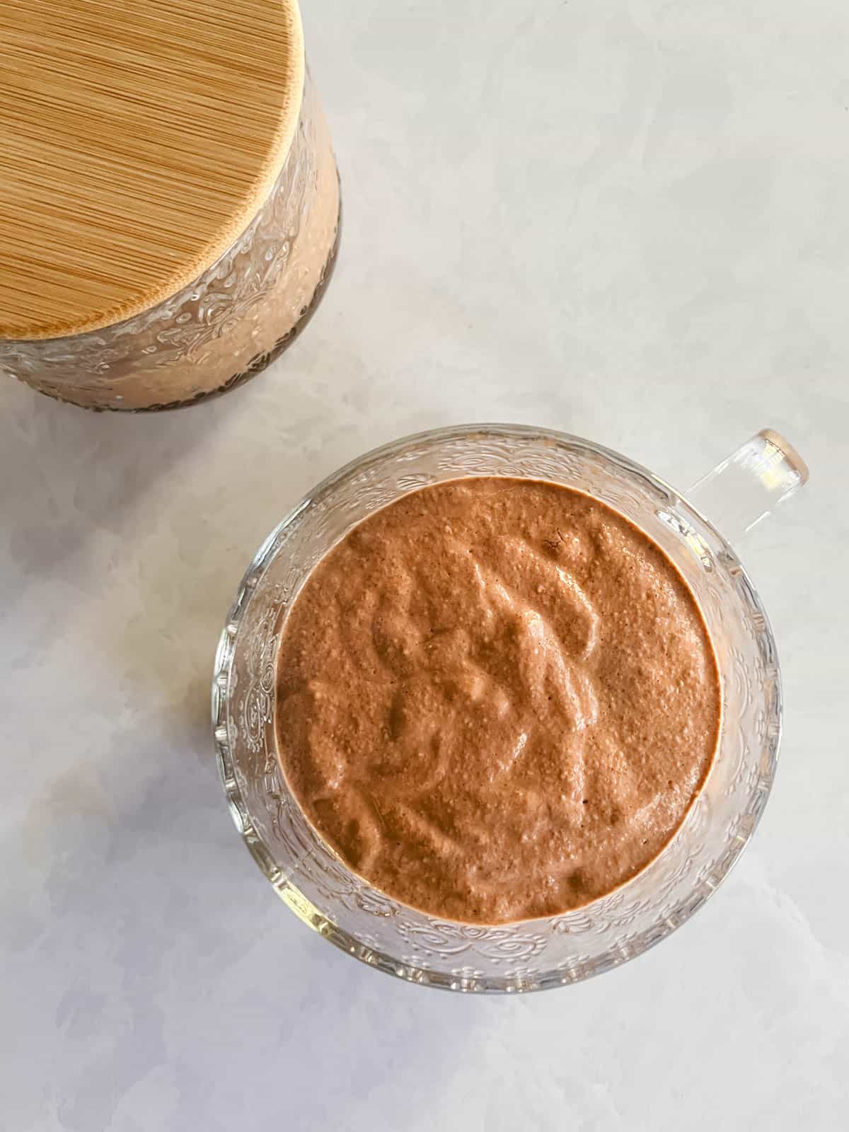 glass mug containing creamy blended chocolate peanut butter overnight oats with covered glass mug in the background