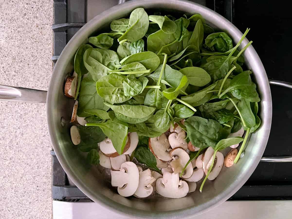 large skillet containing spinach and sliced mushrooms