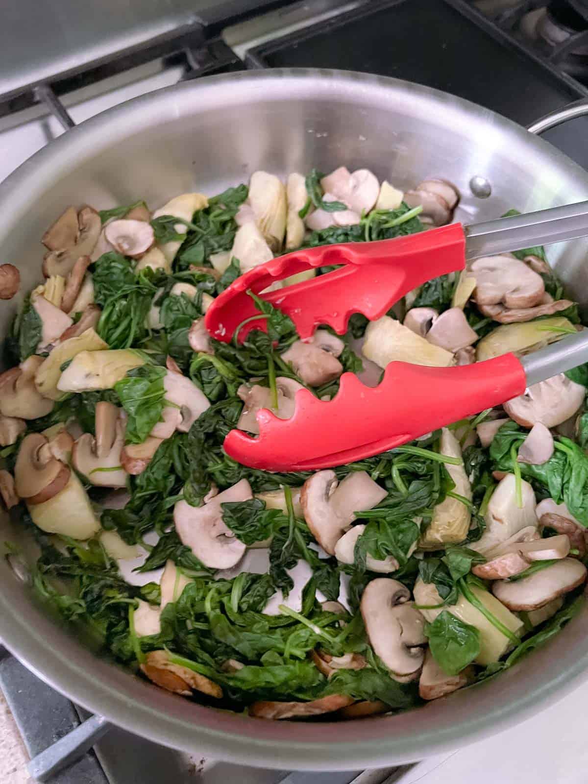 skillet containing sautéed spinach, mushrooms, and artichokes