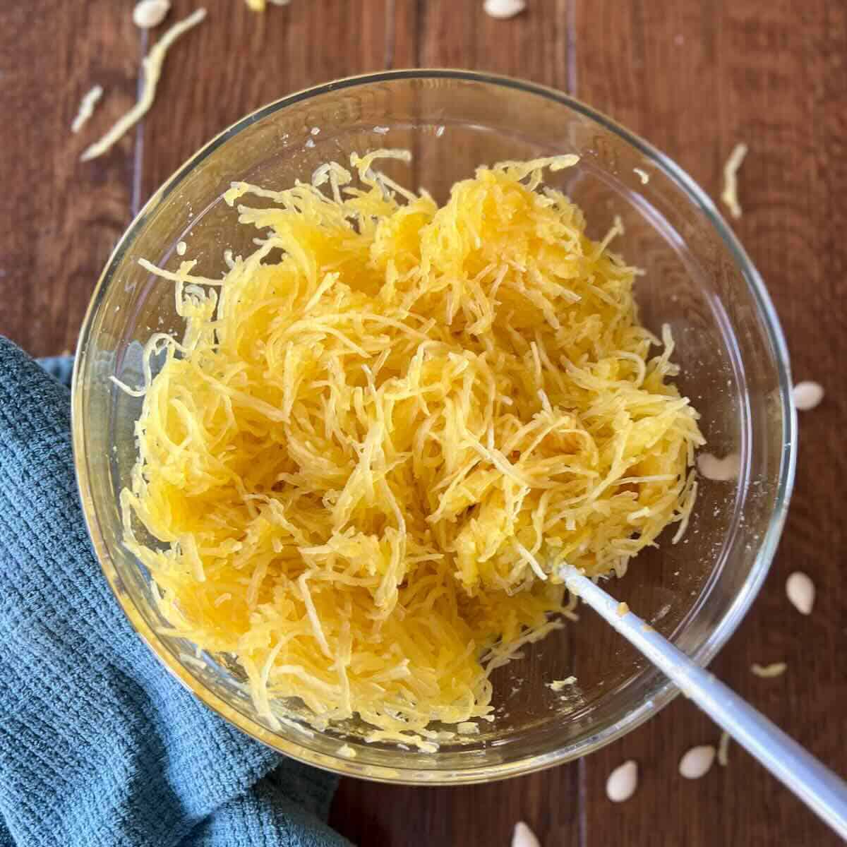 close up of bowl of cooked spaghetti squash with fork and napkin