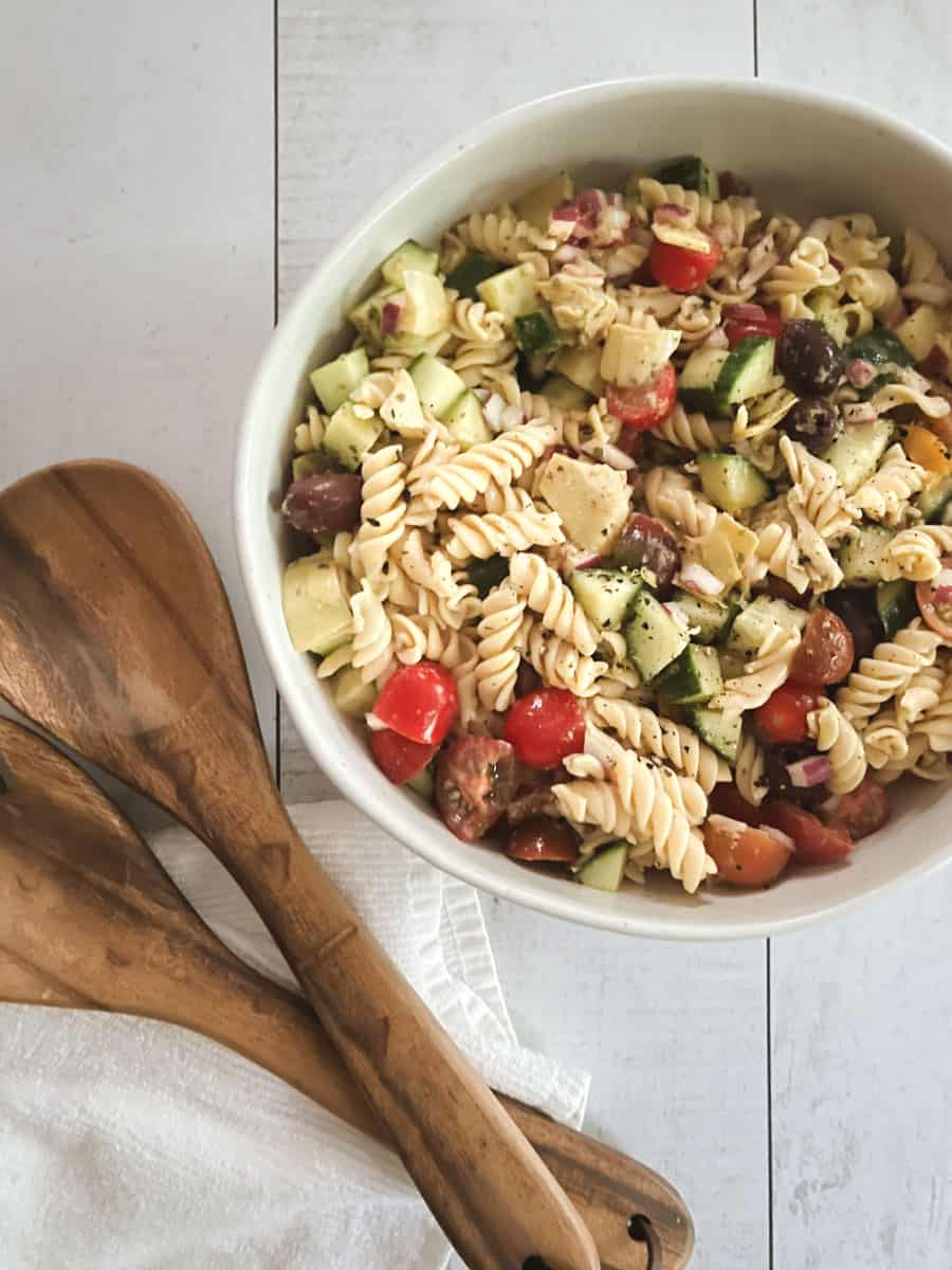 bowl of healthy vegan pasta salad with wooden serving tongs