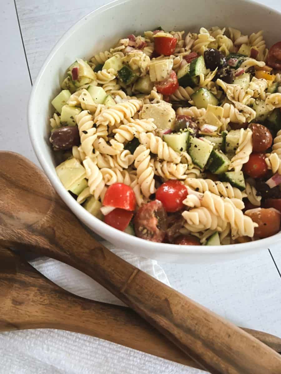 close up of bowl of healthy vegan pasta salad with wooden serving tongs