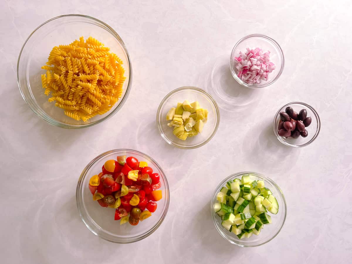 bowls containing ingredients for healthy vegan pasta salad