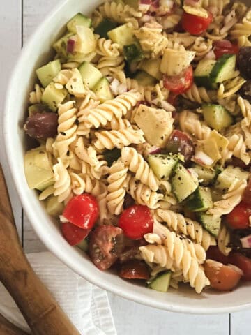 close up of oil-free healthy vegan pasta salad in a bowl with wooden serving tongs