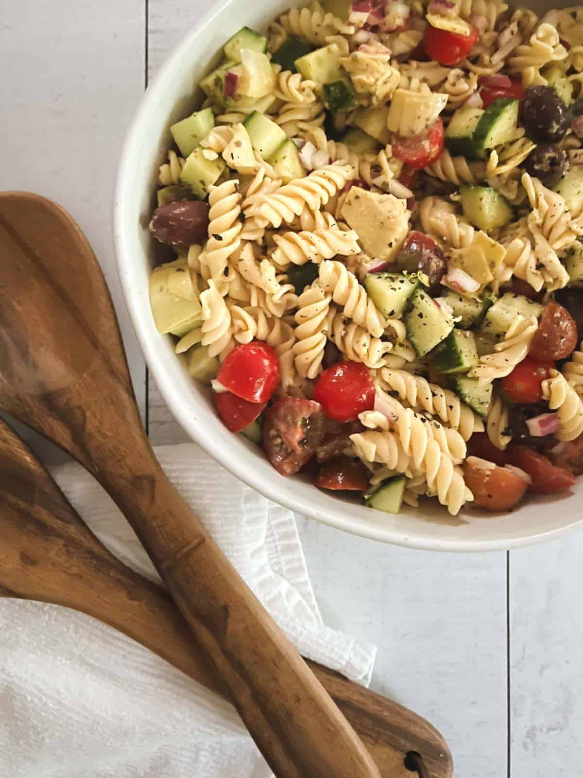 close up of bowl of healthy vegan pasta salad with wooden serving tongs and napkin