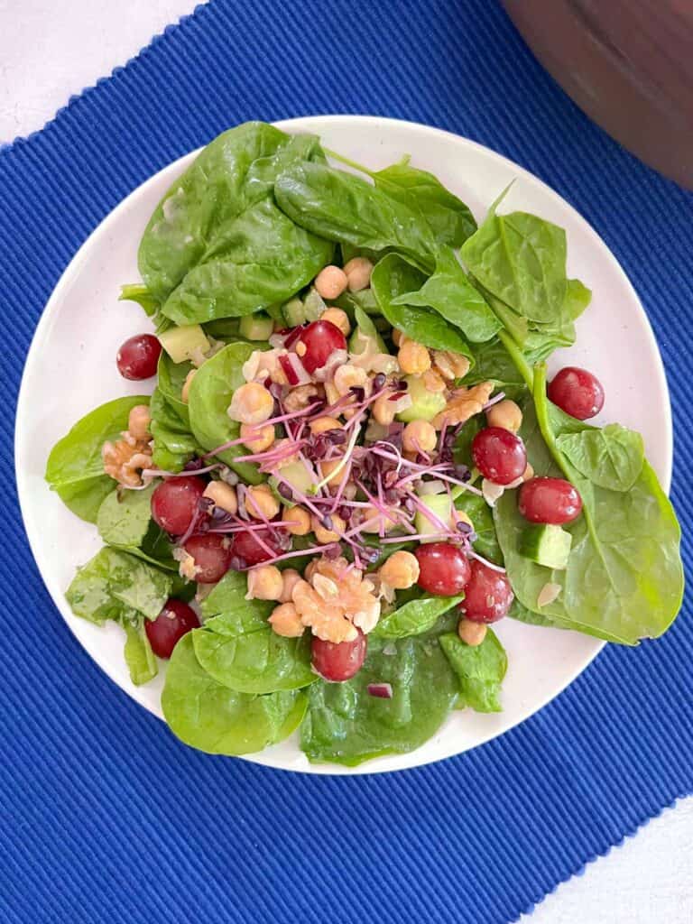 plate of Mediterranean salad topped with micro greens on a blue cloth placemat