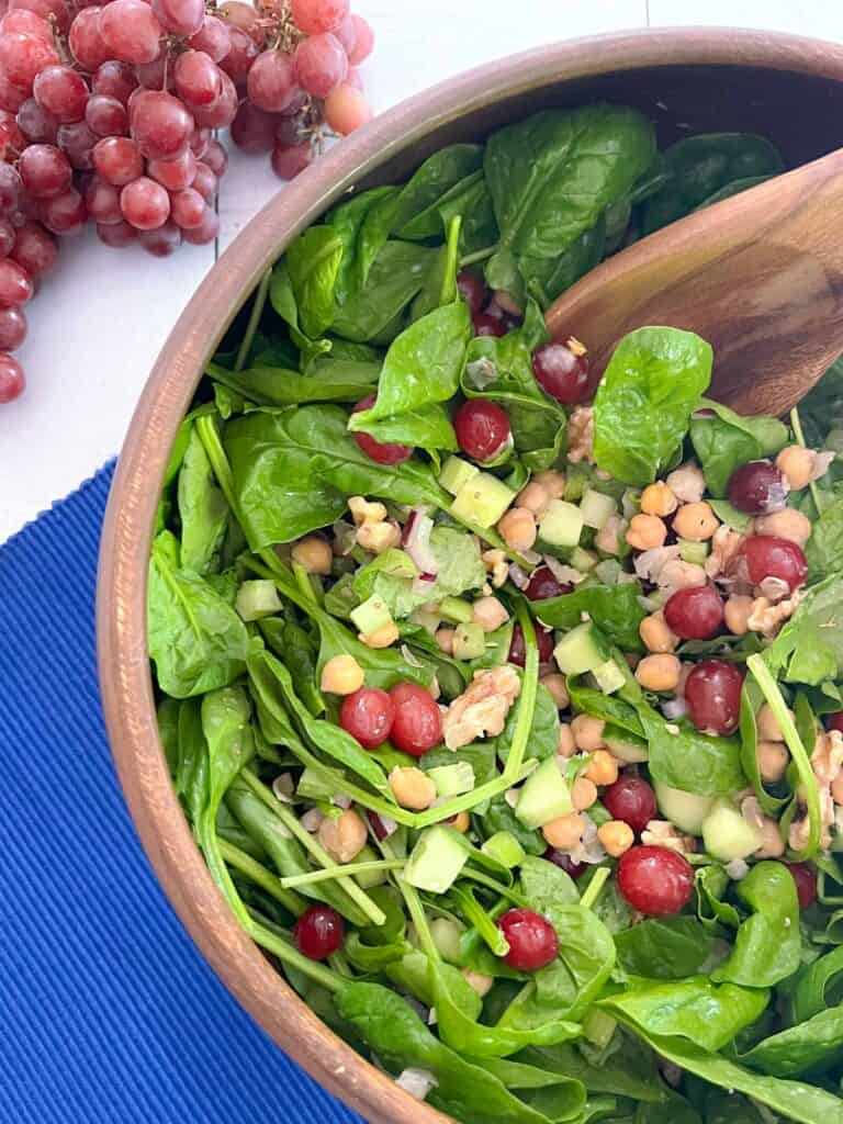 close up of Mediterranean salad in wooden bowl with spoon; grapes in background