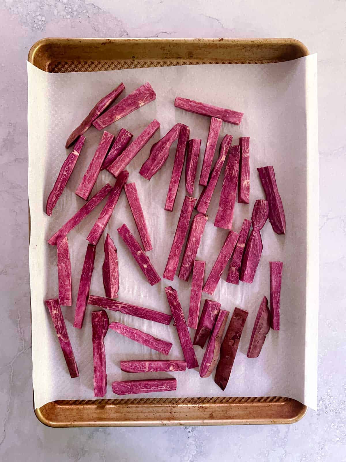 baking sheet with raw purple sweet potatoes arranged on parchment paper