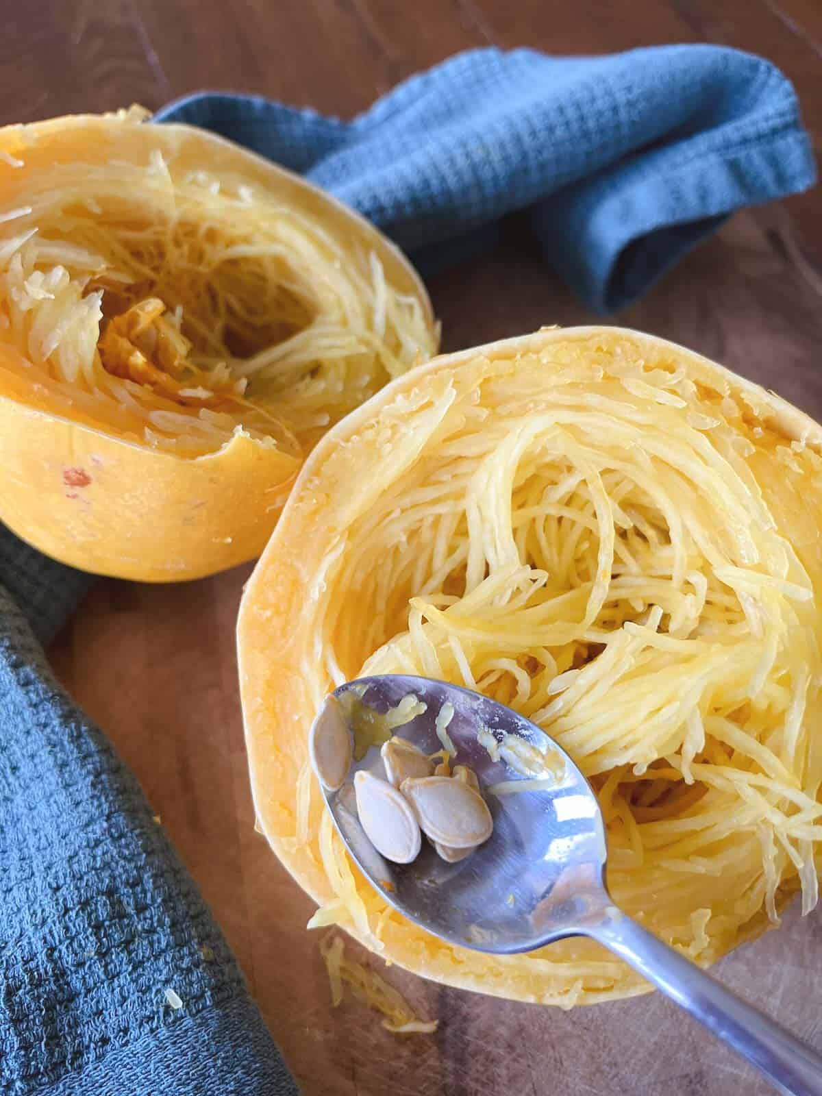 spoon scooping seeds out of halved spaghetti squash