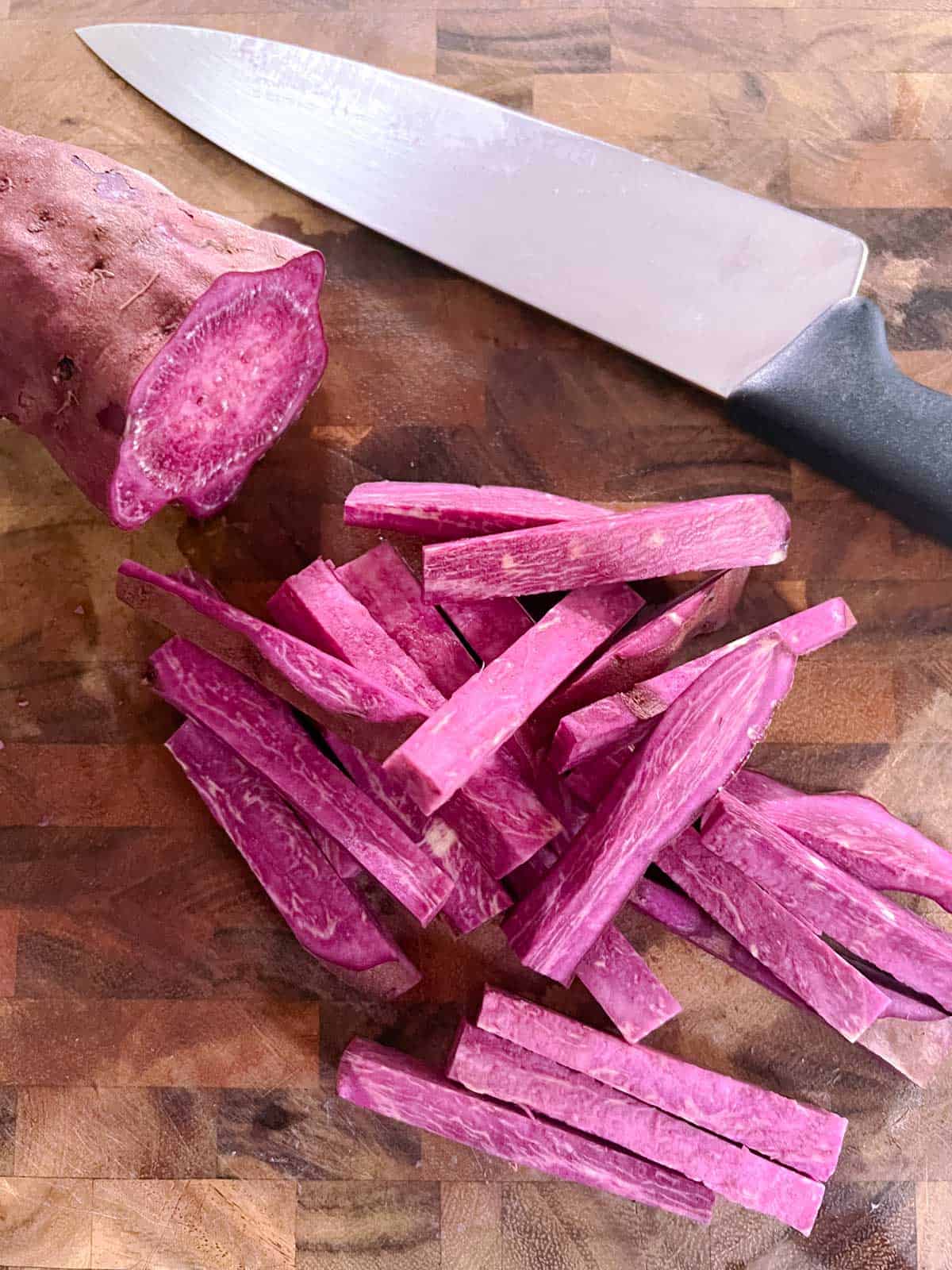 partially sliced purple sweet potato on a cutting board with a knife