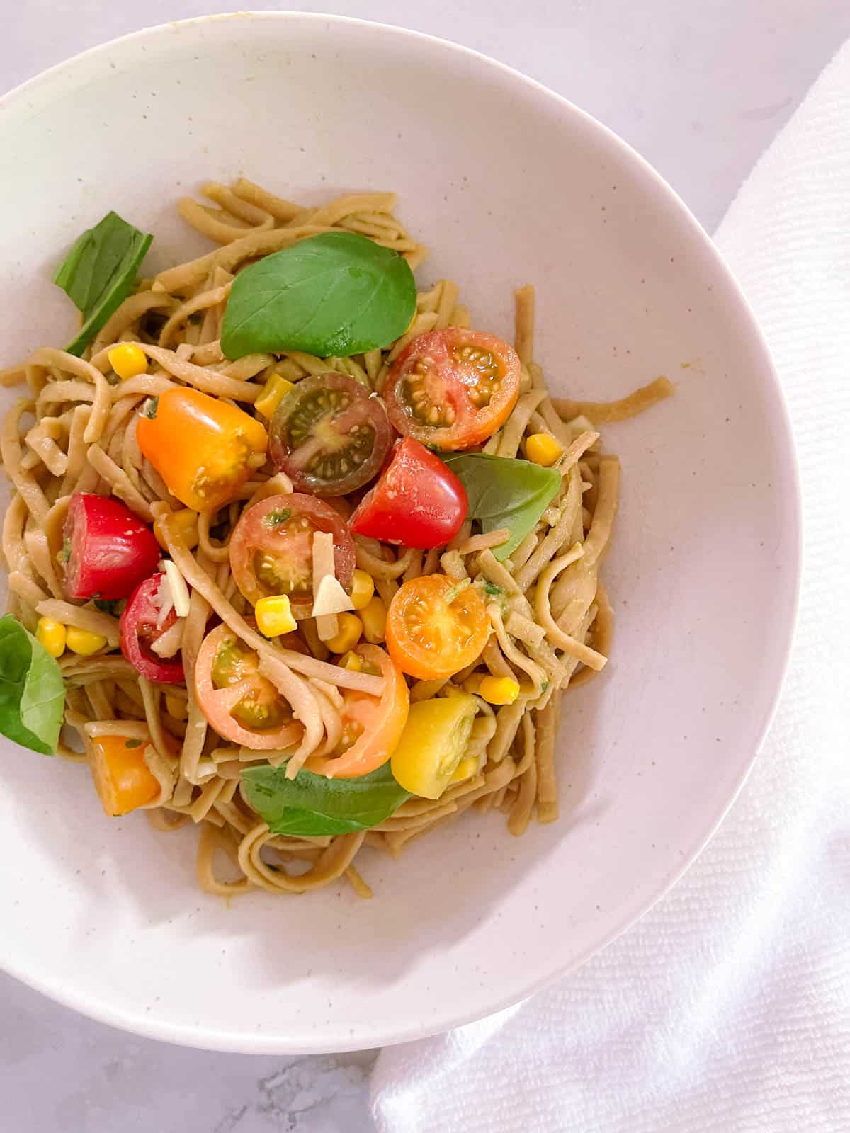 bowl of creamy avocado basil pasta with tomatoes and corn with napkin tucked underneath