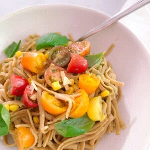 close up of creamy avocado basil pasta with tomatoes and corn in a bowl with a spoon