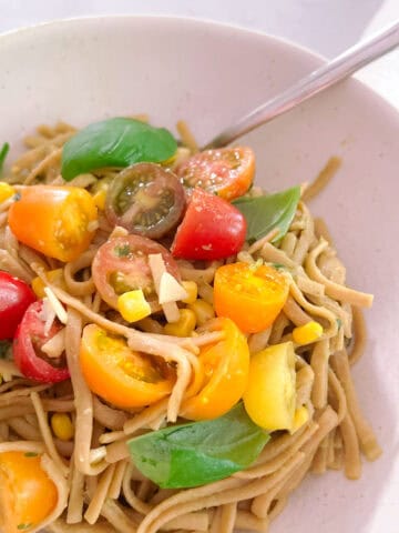 close up of creamy avocado basil pasta with tomatoes and corn in a bowl with a spoon